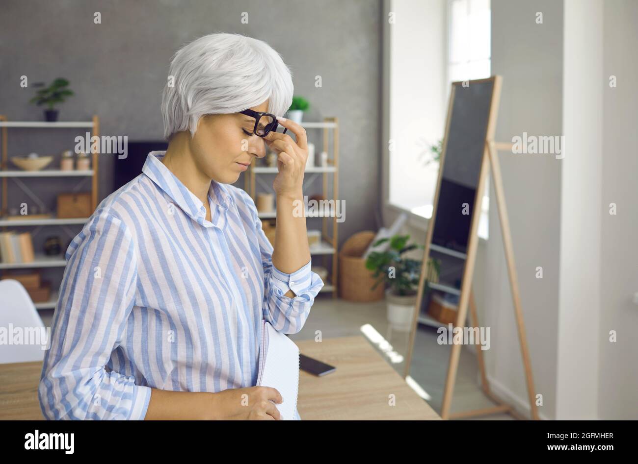 Müde stressige reife Geschäftsfrau, die an Augenmüdigkeit und Kopfschmerzen bei der Arbeit leidet. Stockfoto