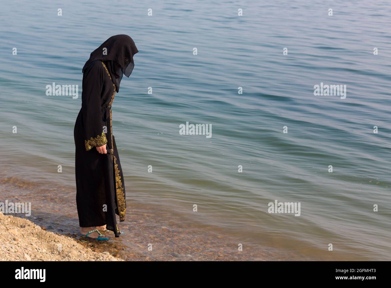 Eine muslimische Frau in nationaler Kleidung strebt ihre Füße ins Meer. Stockfoto