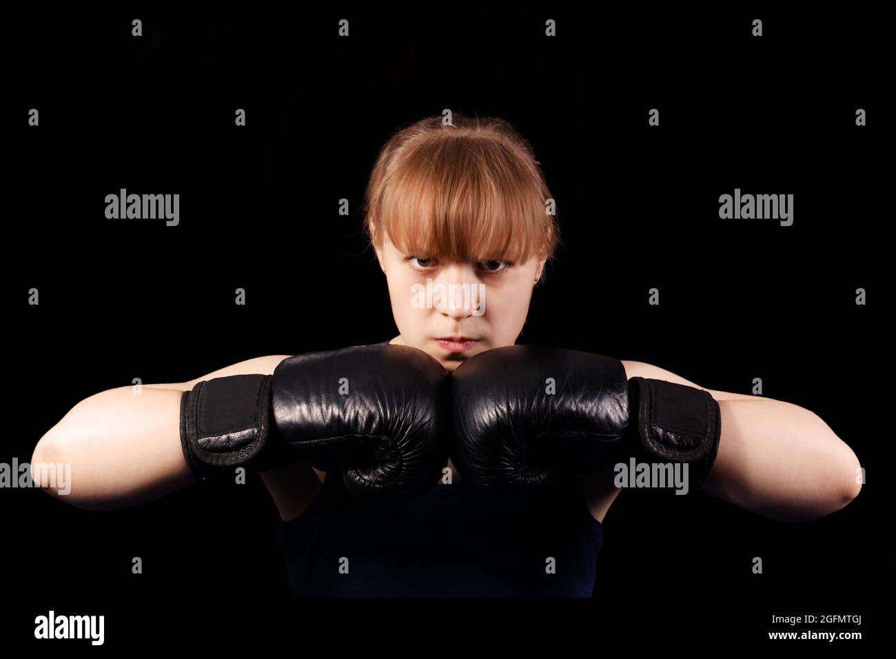 Porträt eines jungen Boxermädchen, das die Hände in schwarzen Boxhandschuhen vor schwarzem Hintergrund zusammenstellt Stockfoto