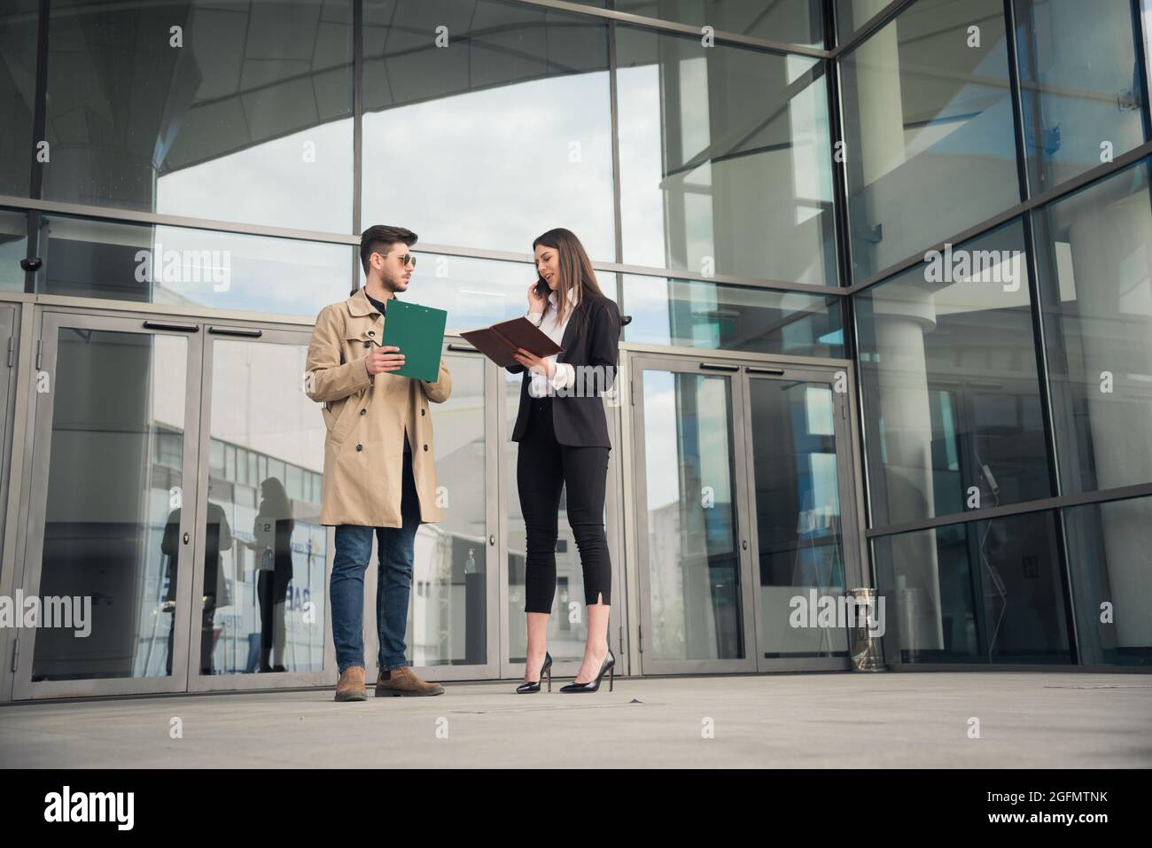 Die Chefin spricht am Telefon und schaut sich die Pläne an, während ihre Assistenzin auf sie wartet Stockfoto