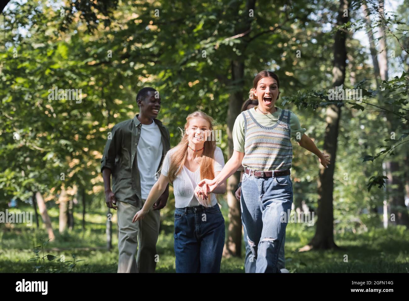 Fröhliche Teenager-Mädchen laufen in der Nähe von multiethnischen Freunden im Park Stockfoto