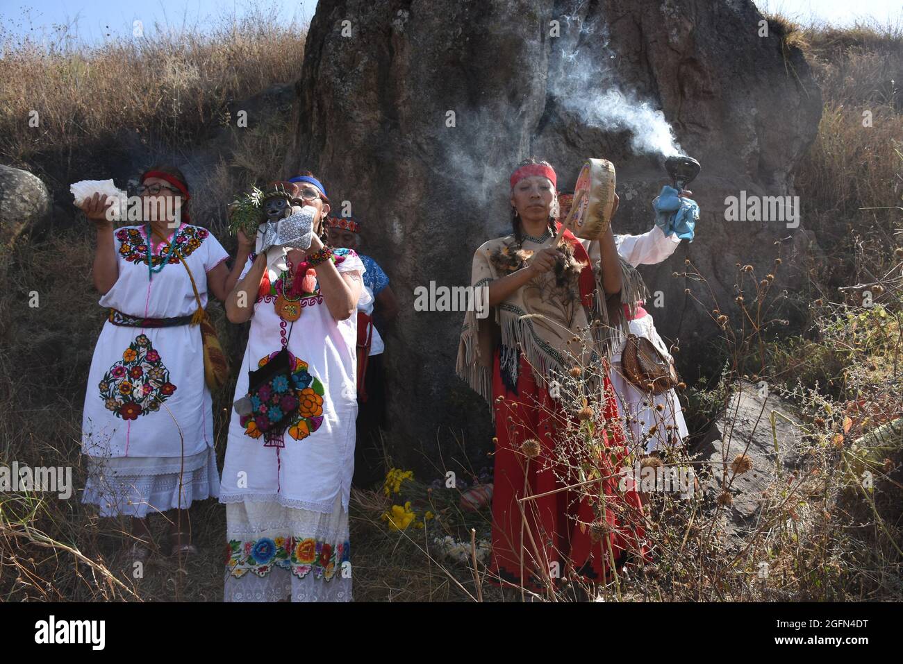 Curanderas – traditionelle Heiler oder Schamanen – führen ein Ritual vor einem Felsblock mit einer Schnitzerei von Xipe Totec, dem aztekischen gott der Landwirtschaft, durch. Stockfoto