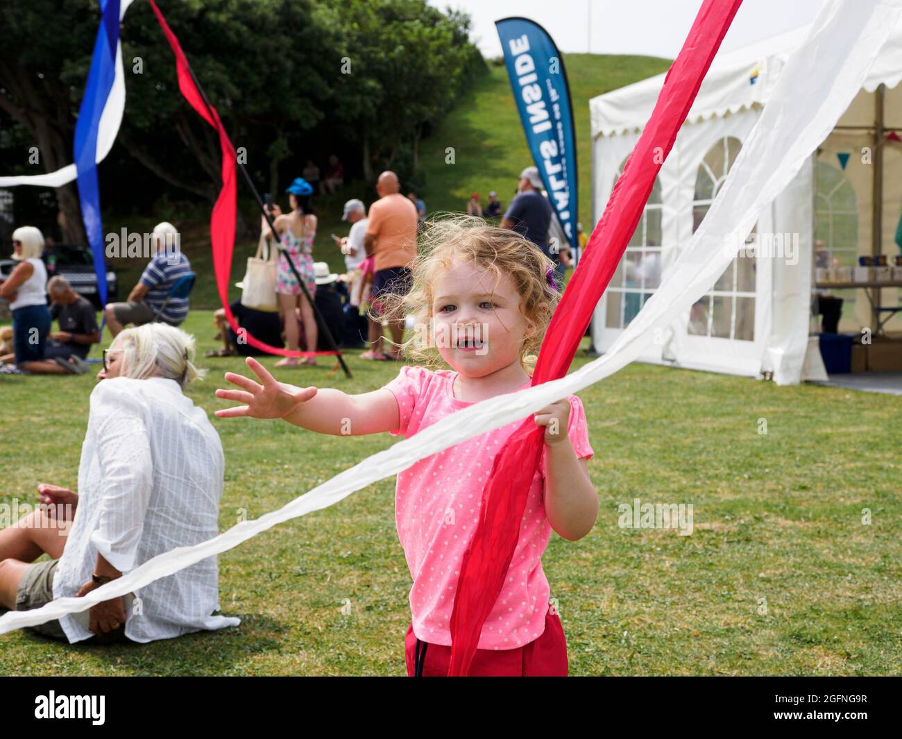Kleines Kind, das beim Festival in Cornwall, Großbritannien, mit Fahnenbändern spielt Stockfoto