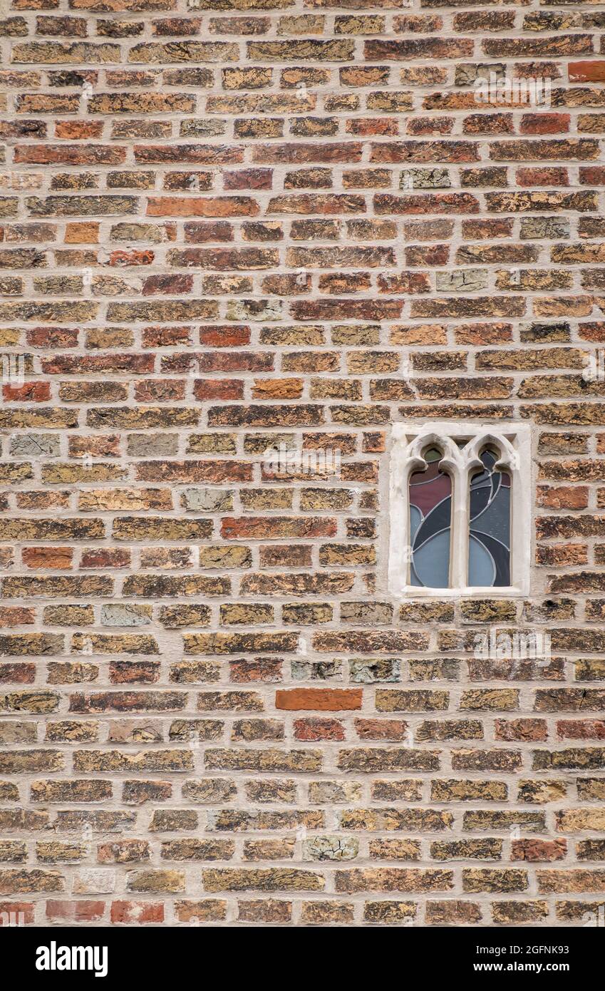 Brügge, Flandern, Belgien - 4. August 2021: Kleinstes Spionagefenster mit Glasmalerei in brauner Ziegelmauer des Gruuthuse-Palastes. Stockfoto