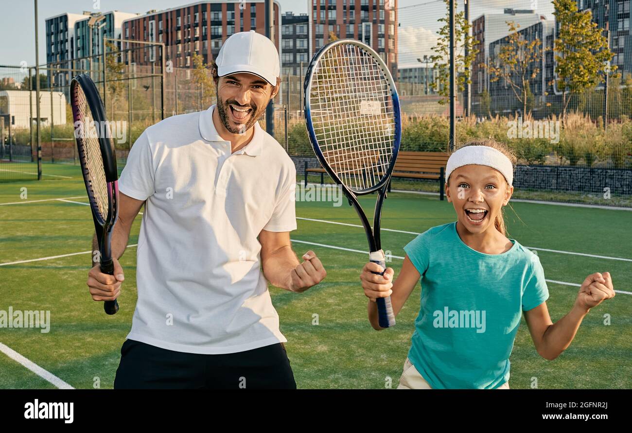 Tennistrainerin mit weiblichem Kind feiert auf dem grünen Platz ein gewinnendes Tennisspiel. Tennistraining für Kinder Stockfoto