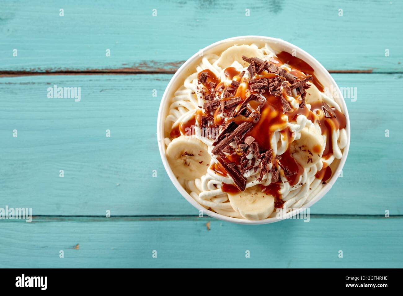 Köstliche Spezialität deutsches Dessert aus Eis-Spaghetti mit Schokoladenflocken, Karamellsauce und frischer Banane von oben auf einem blauen Blick gekrönt Stockfoto