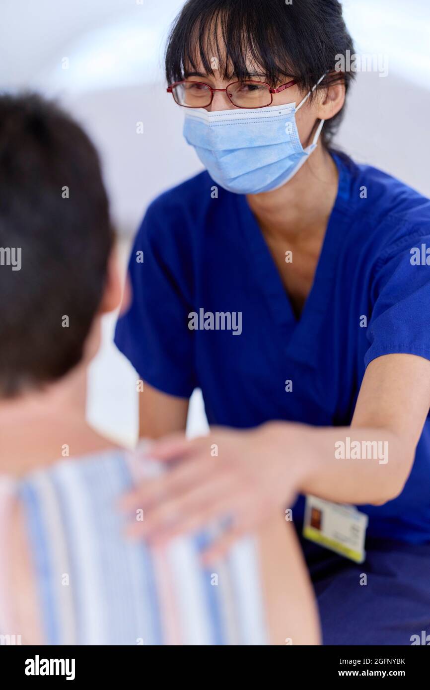 Krankenschwester mit PSA-Maske im Gespräch mit dem Patienten Stockfoto