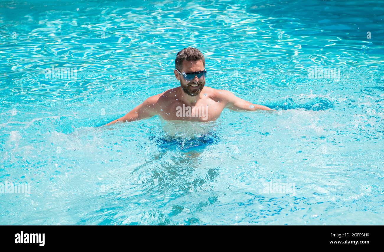 Fröhlicher, schöner Mann in einer Brille, der im Sommer im Pool schwimmend ist, Spa Stockfoto