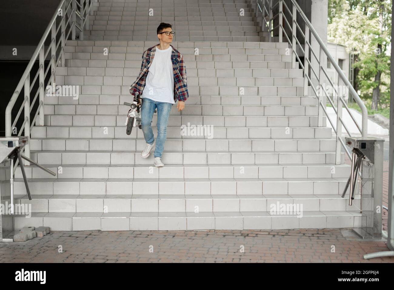 Ein Student steigt mit einem Elektroroller die Treppe zur Universität hinab. Modernes Stadtkonzept. Ökologischer technologischer Lebensstil. Stockfoto