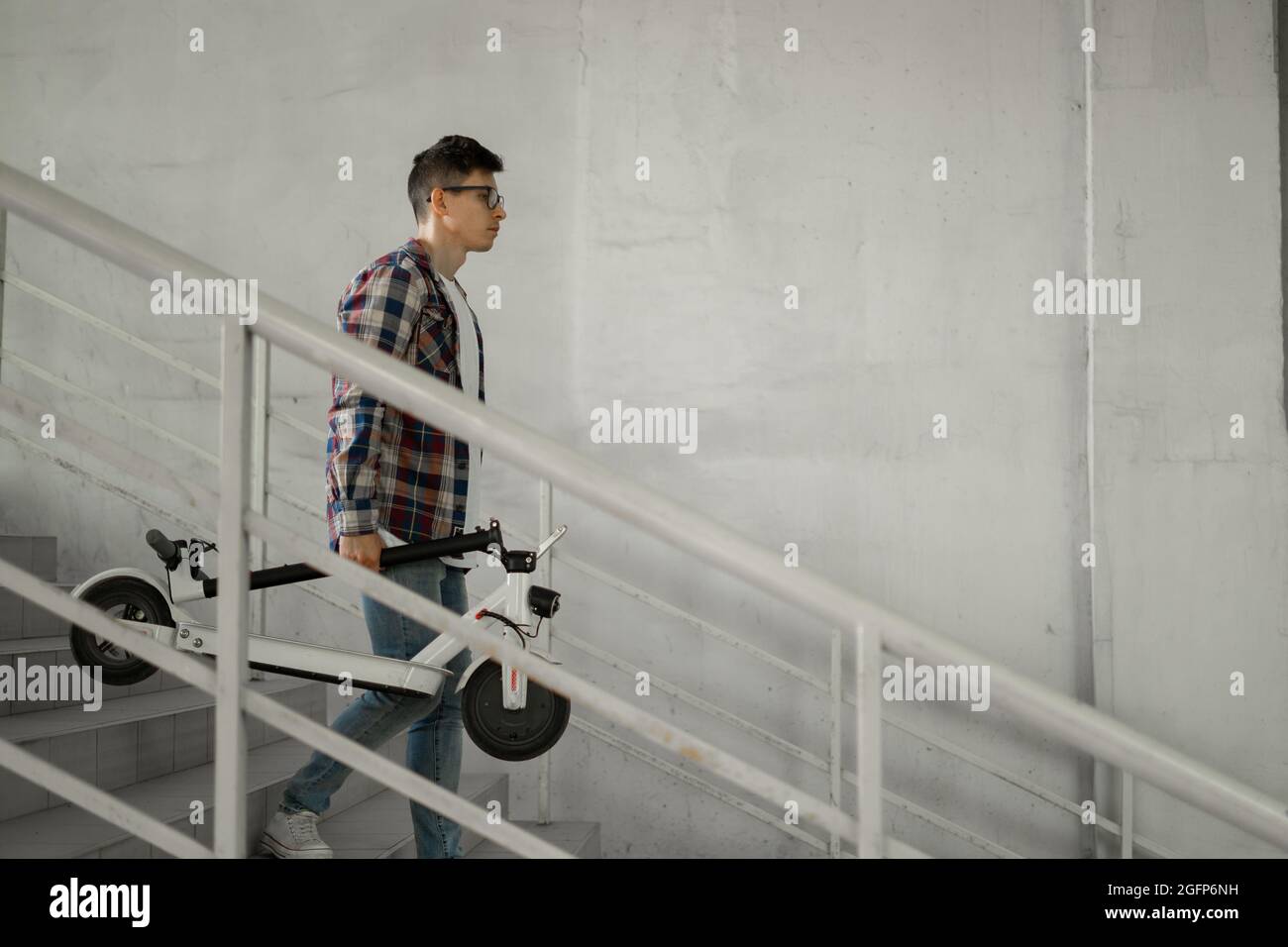 Ein Student steigt mit einem Elektroroller die Treppe zur Universität hinab. Modernes Stadtkonzept. Ökologischer technologischer Lebensstil. Stockfoto