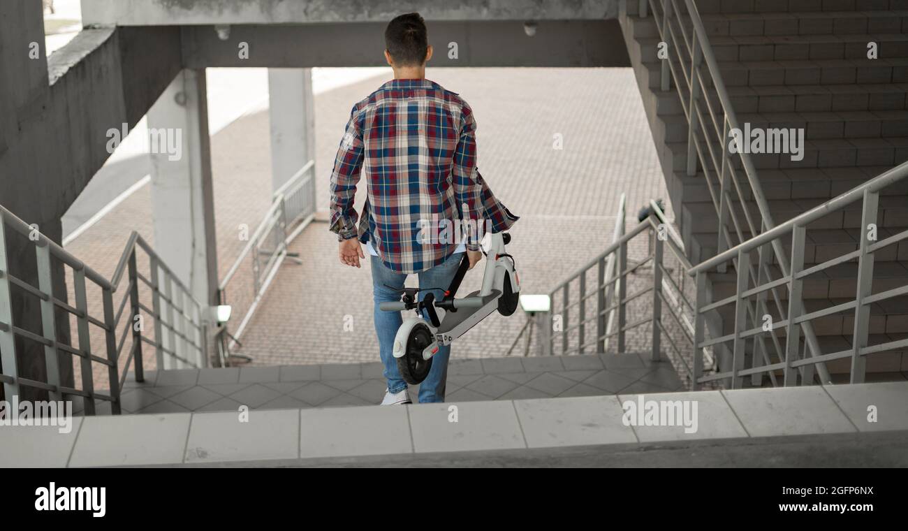 Ein Student steigt mit einem Elektroroller die Treppe zur Universität hinab. Modernes Stadtkonzept. Ökologischer technologischer Lebensstil. Stockfoto