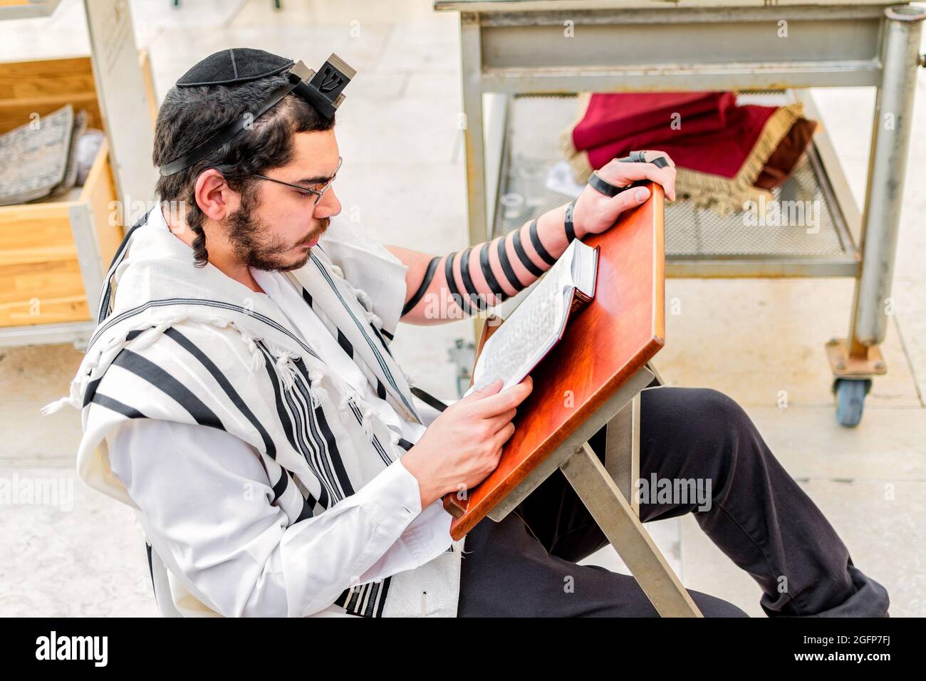 Junger jüdischer Mann, der einen Schal trägt und die heiligen Tefillin-Schriften an der Westmauer lernt Stockfoto