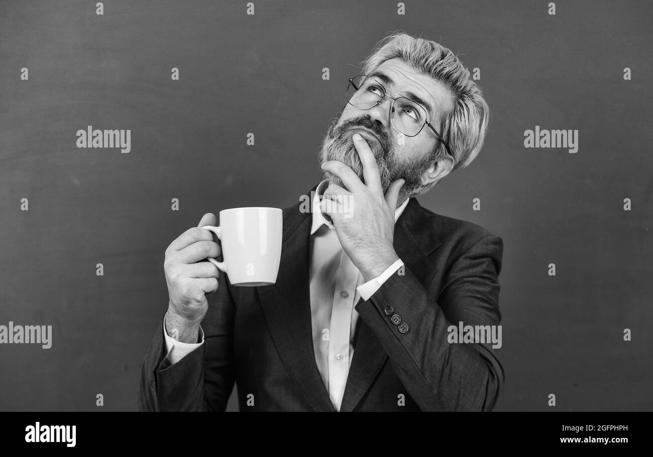 Wenn Sie es träumen können, können Sie es tun. Älterer Träumer mit nachdenklicher Optik. Bärtiger Mann träumt davon, Tee zu trinken. Nachdenklicher Lehrer hält Kaffeetasse. Schule Stockfoto