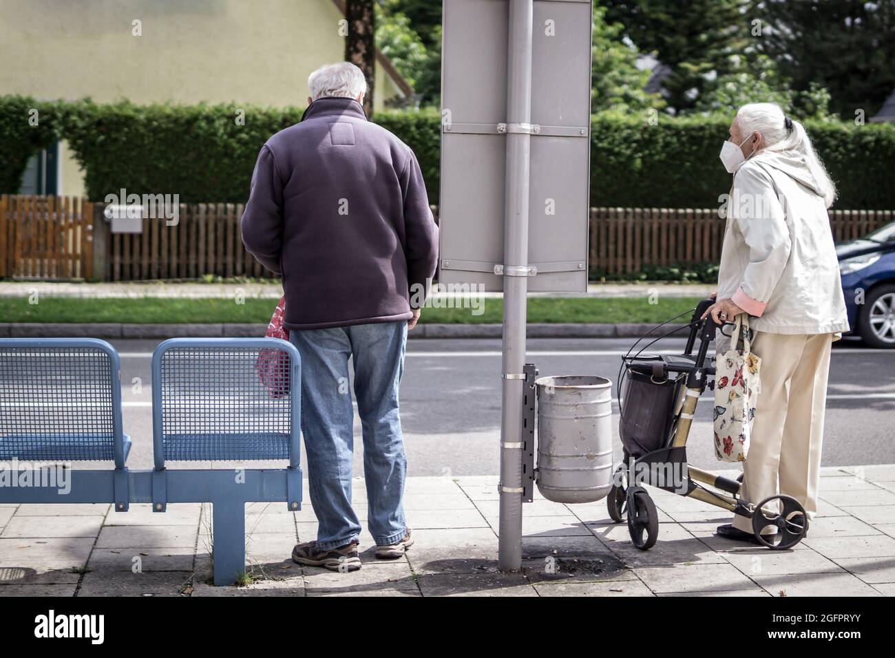 Zwei alte Leute warten am Busbahnhof auf die Ankunft des Busses. Die Frau hat einen wandenden Collator als Stütze. Stockfoto