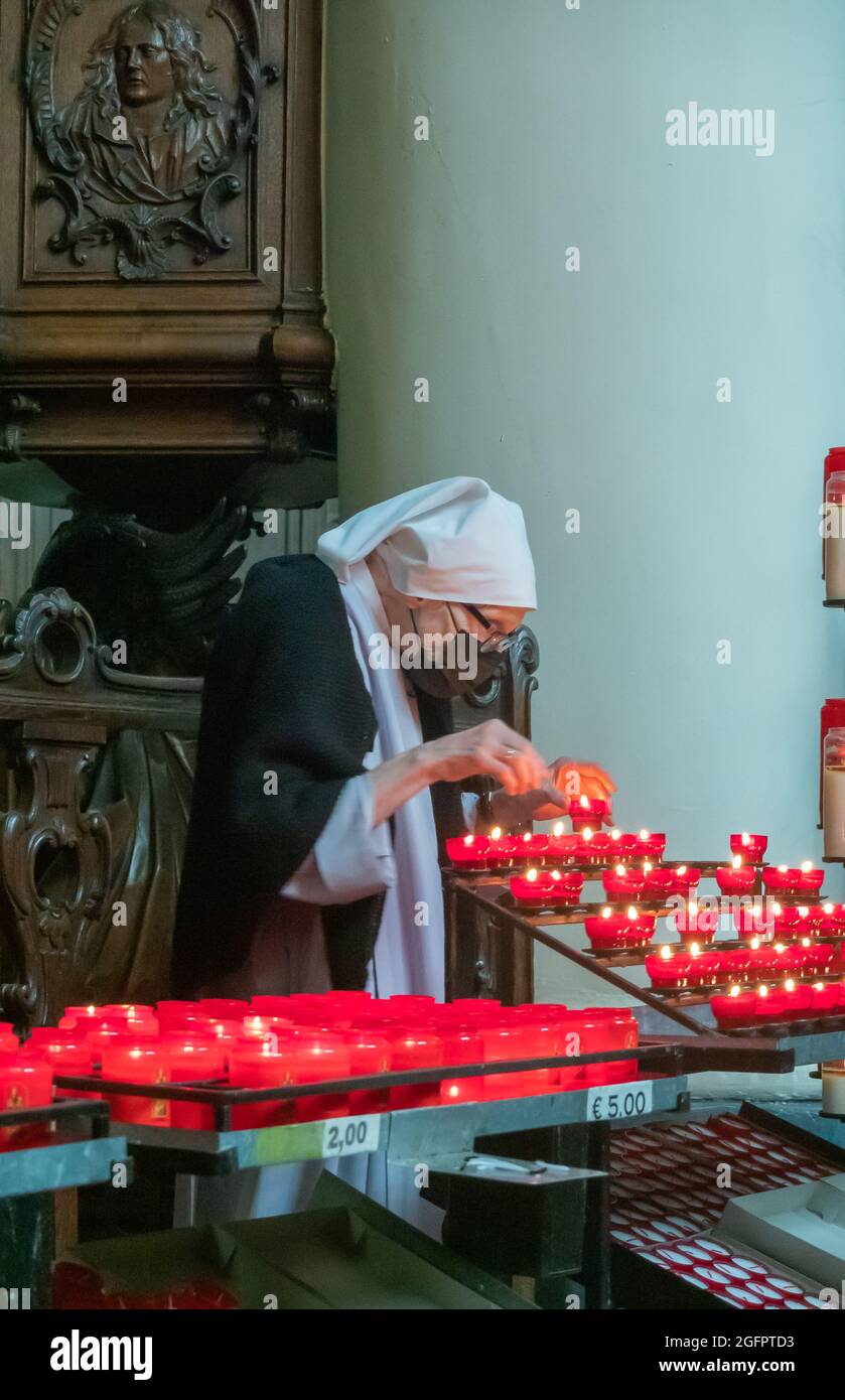 Brügge, Flandern, Belgien - 4. August 2021: Beguinage-Kirche. Nonne entfernt brennende Kerzen, bezahlt von Gläubigen, die noch nicht ausgebrannt sind. Stockfoto