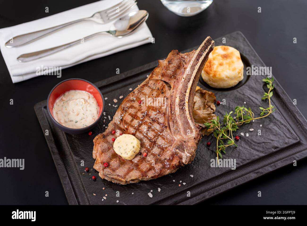 Gegrilltes Kalbsschnitzel auf schwarzem Steinteller mit Sauce und Garnitur. Stockfoto