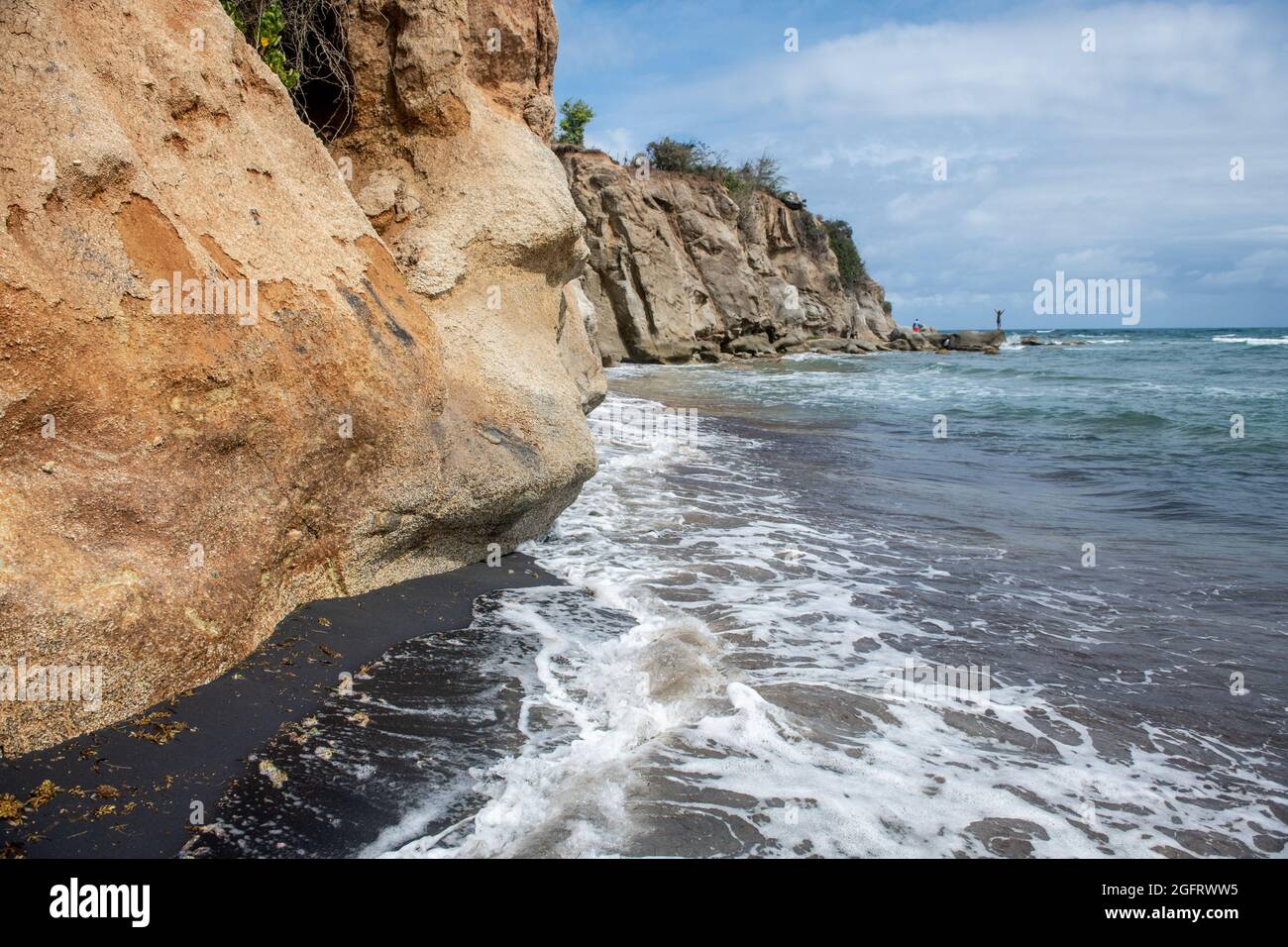 Wasser rauscht über schwarzen Sand unter einer Klippe - Puerto Rico Stockfoto
