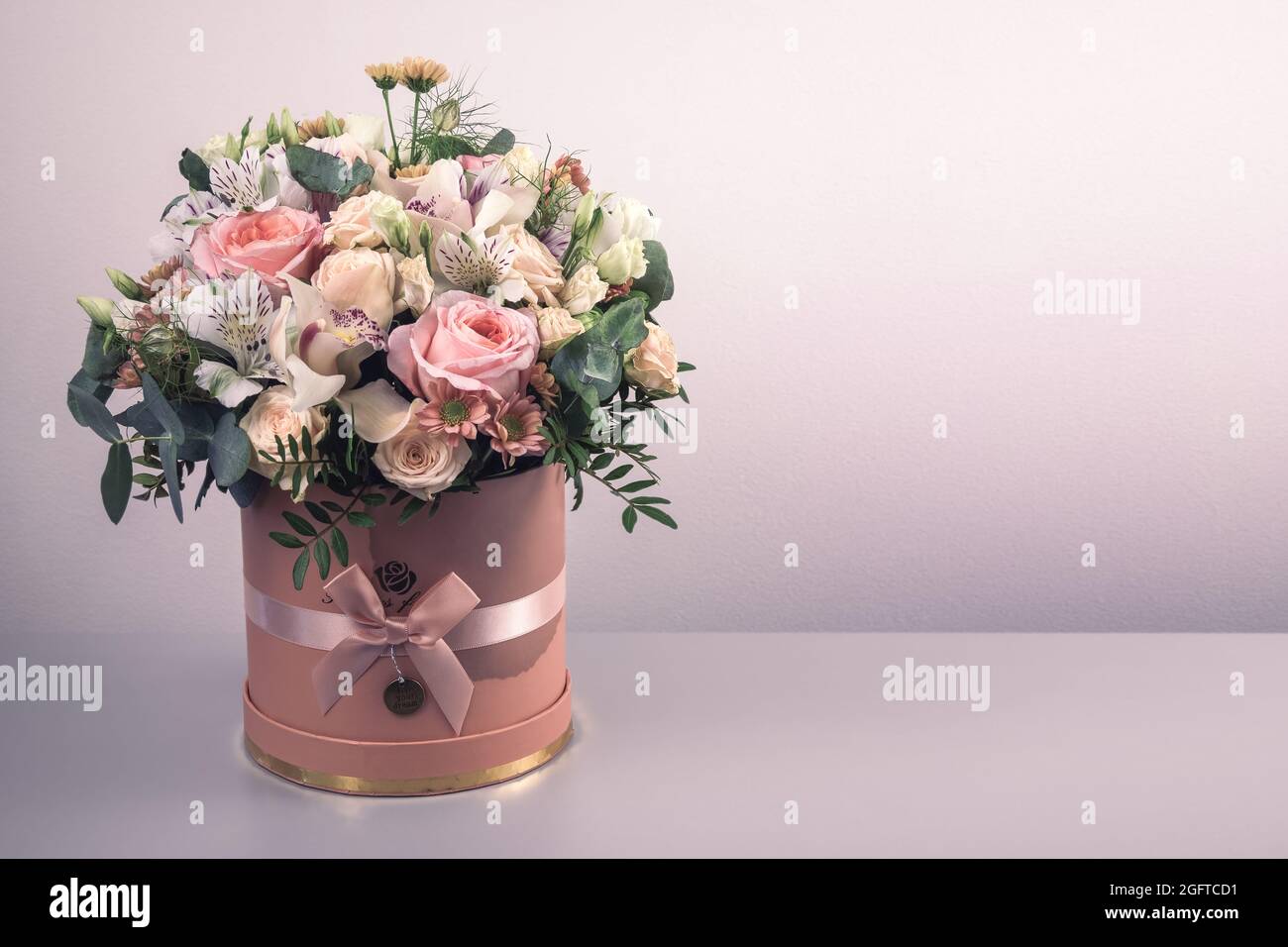 Ein schöner Strauß zarter Blüten aus rosa Rosen, weißen Lilien und gelben Gerberas in einer handgefertigten Schachtel. Alles ist mit grünen palmenlea dekoriert Stockfoto