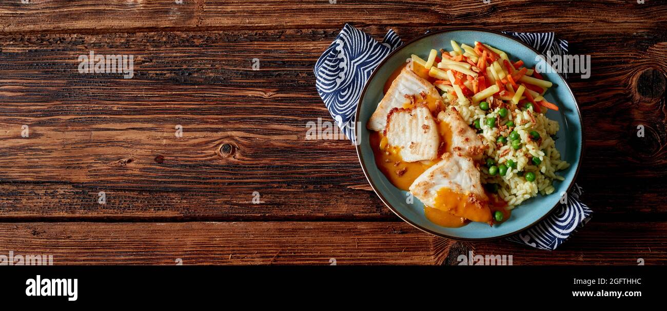 Filets von Cichliden Fisch mit Reis und Erbsenmischung und Karotten mit Pastinaken in einer Buttersauce auf einem Teller über einem rustikalen Holzbrett Hintergrund serviert wi Stockfoto