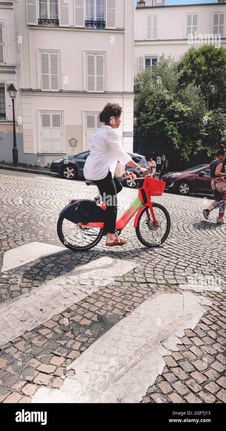 Paris, Frankreich - Juli 2021: Elegante Frau mit weißem Hemd und schwarzer Hose auf einem gemieteten Lime-E-Bike von Uber bergab in Montmartre in Paris. Stockfoto