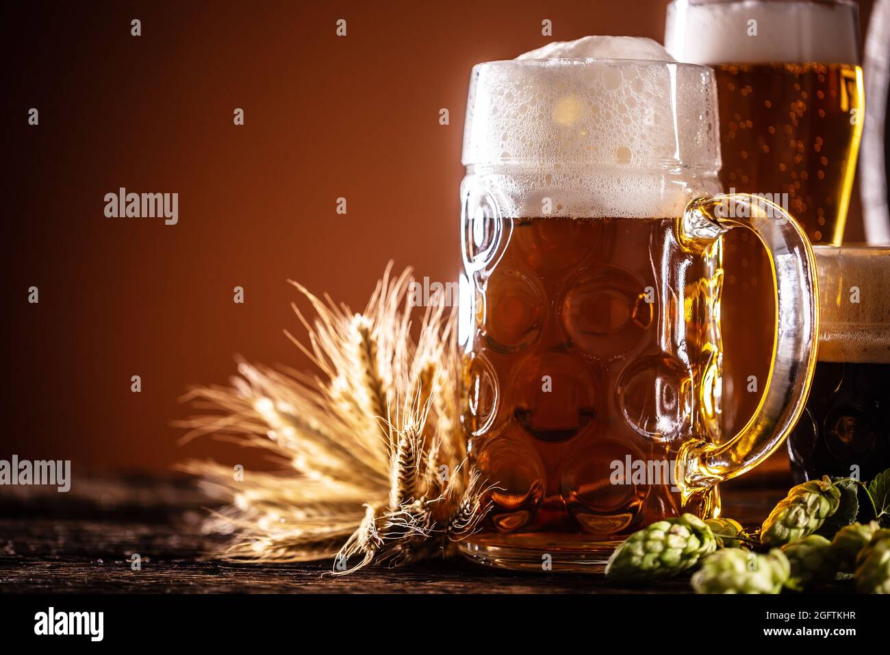 Ein Liter Glas Bier vom Fass daneben zwei kleinere Biere vor einem Holzfass als Dekoration aus Gerste und Hopfen. Stockfoto