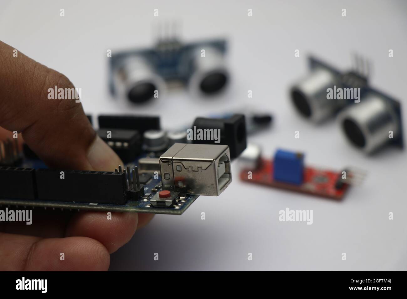 Kreativer Ingenieur, der Mikrocontroller-Platine hält, die mit verschiedenen anderen Arten von Sensoren im Hintergrund programmierbar ist Stockfoto
