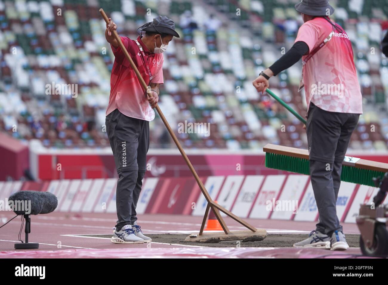 Tokio, Japan. August 2021. Paralympics: Leichtathletik, Weitsprung, im Olympiastadion. Freiwillige glätten den Sand vor dem Wettkampf. Kredit: Marcus Brandt/dpa/Alamy Live Nachrichten Stockfoto