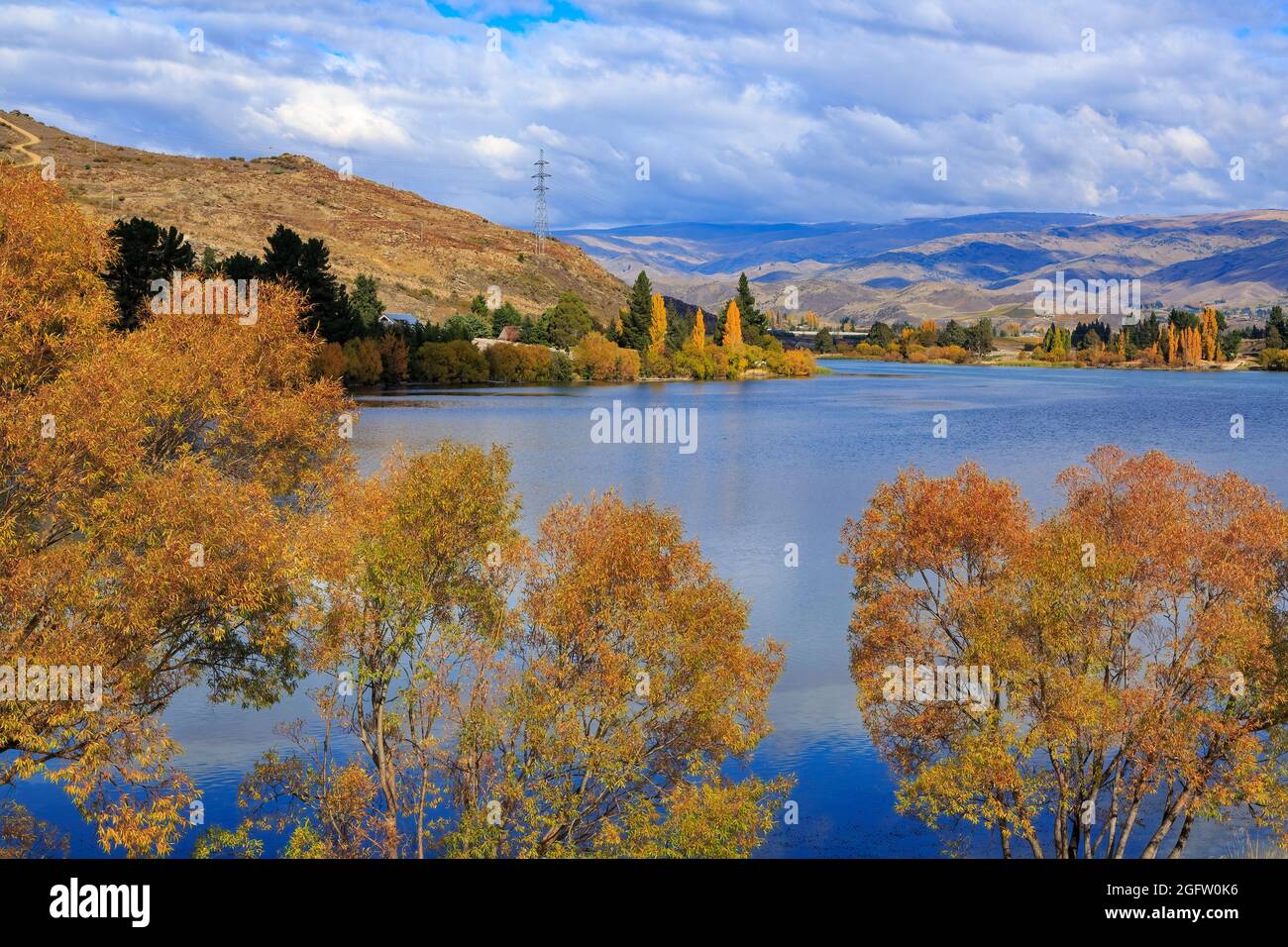 Herbstbäume umgeben das tiefblaue Wasser des Lake Dunstan in Cromwell, Neuseeland Stockfoto
