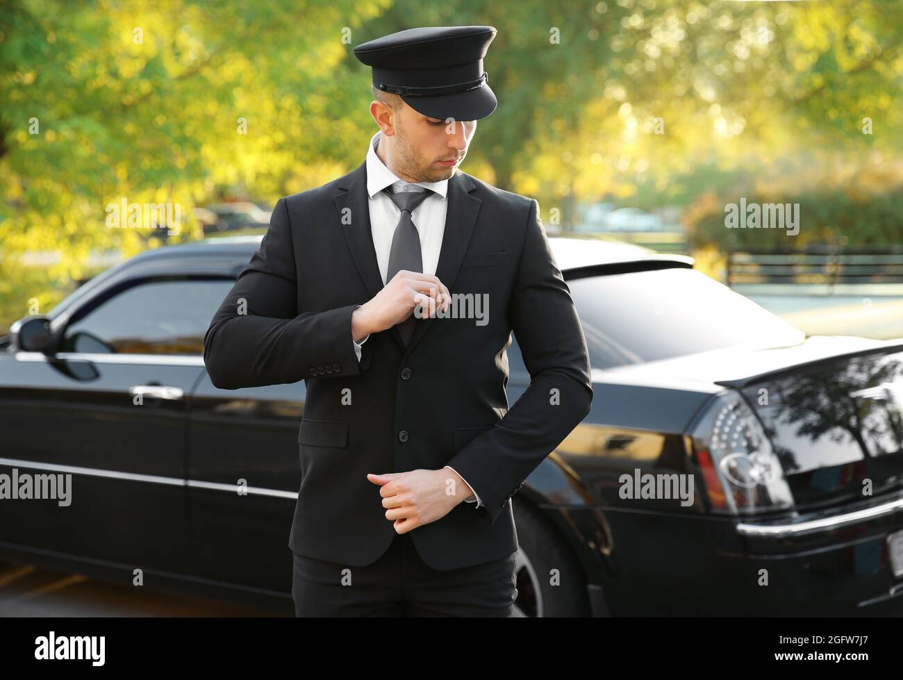 Junger Chauffeur, der den Anzug in der Nähe eines Luxuswagens auf der  Straße anpasst Stockfotografie - Alamy