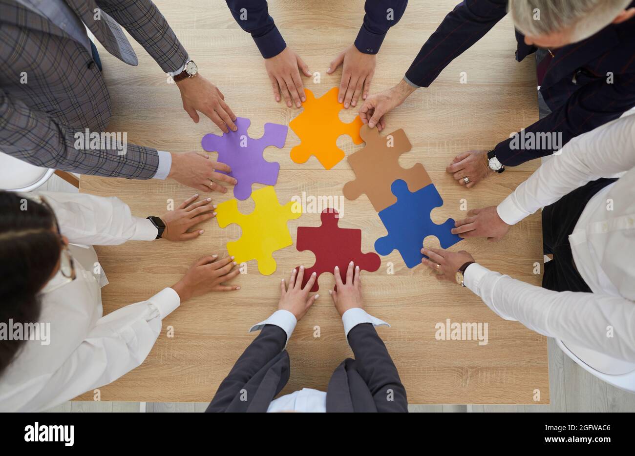 Geschäftsleute, die im Kreis an einem Tisch stehen und zusammen Teile eines farbigen Puzzles machen. Stockfoto