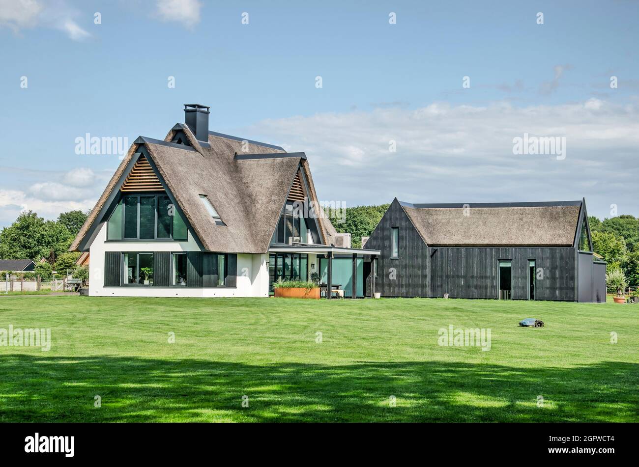 Heino, Niederlande, 7. August 2021: Moderne Villa mit traditionellen Materialien wie Stuck, Holz und einem Strohdach auf einem Rasen, der von einem Roboter kurz gehalten wird Stockfoto