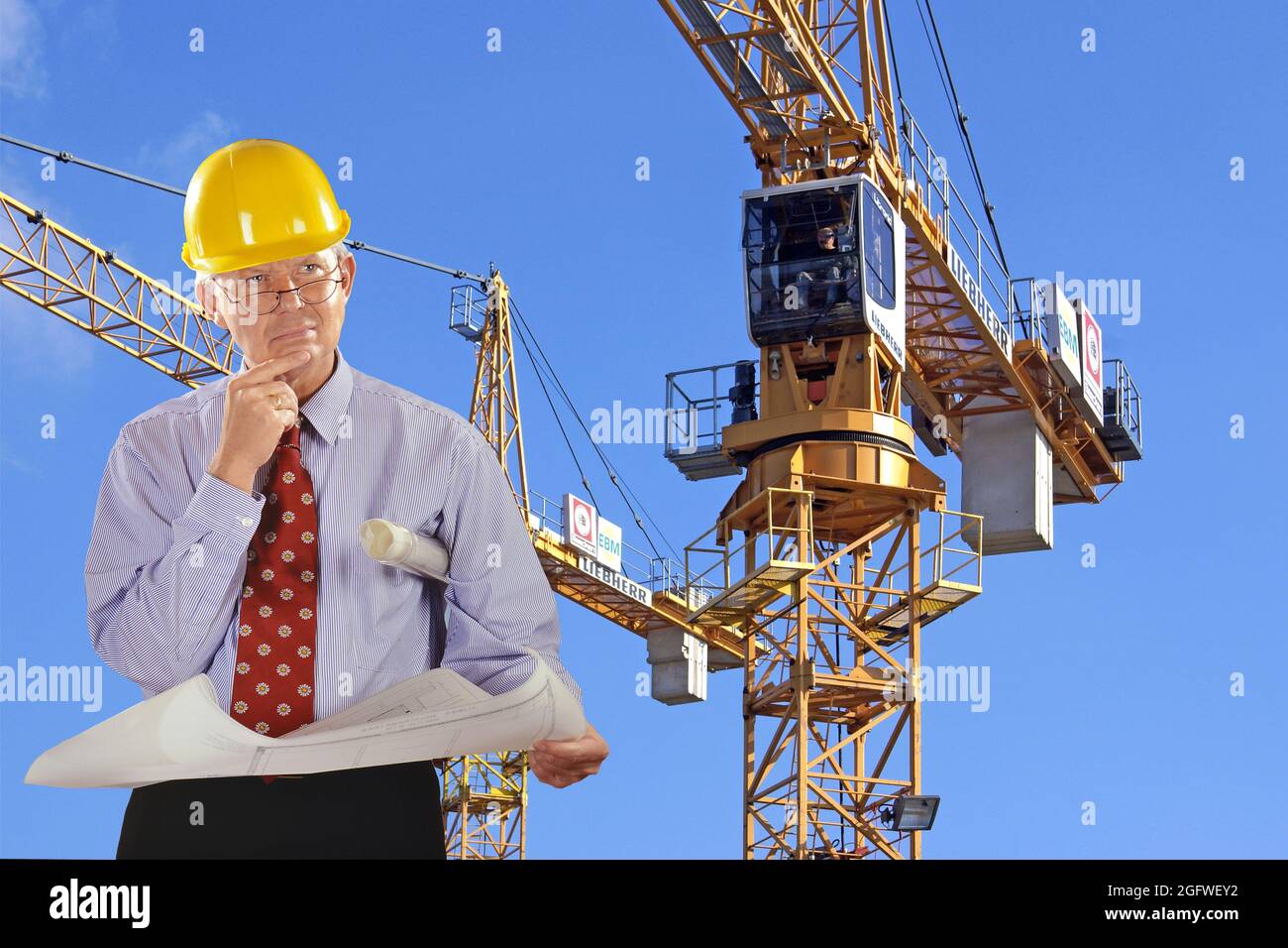 Architekt mit Bauplan und Hut, Turmdrehkran im Hintergrund Stockfoto