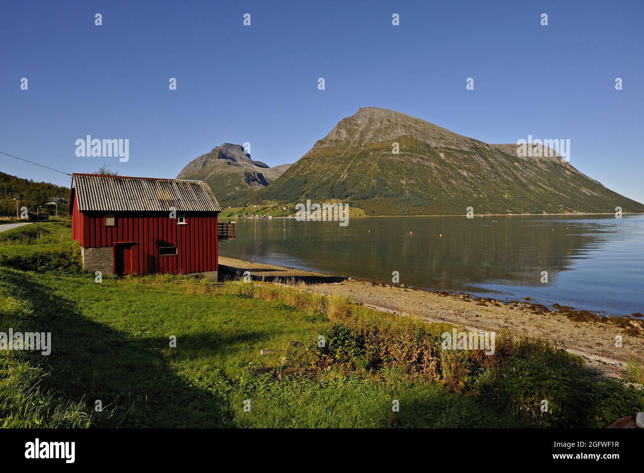 Rotes Holzboathouse in Lia mit der Insel Aldra und den Hjarttinden-Gipfeln dahinter, Norwegen, Haugland, Aldra Island Stockfoto