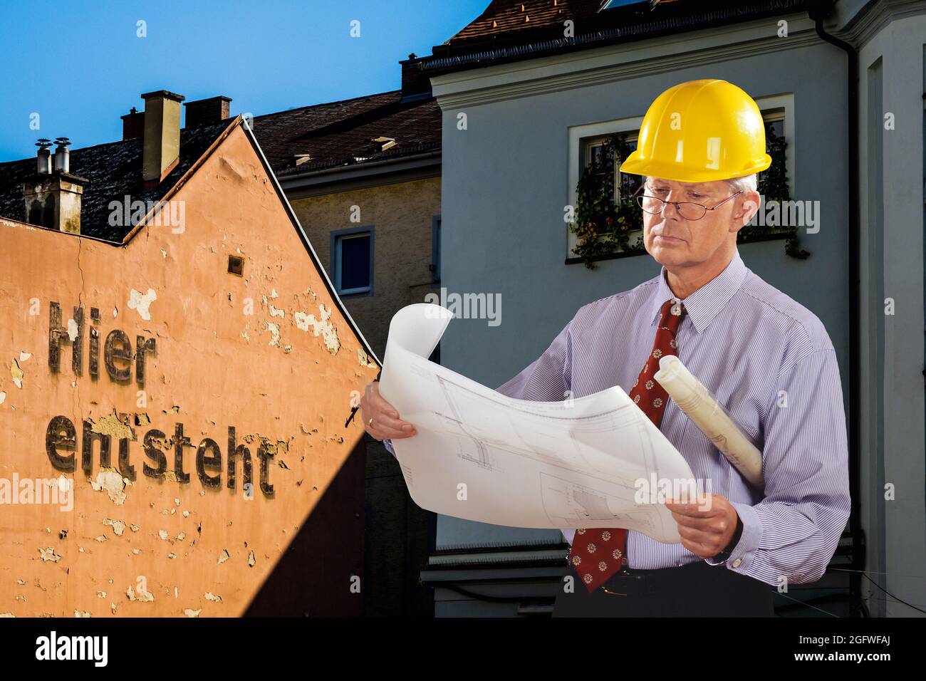 Architekt mit Bauplan und Hut, vor heruntergekommenen Häusern mit der Inschrift: Hier wird gebaut Stockfoto