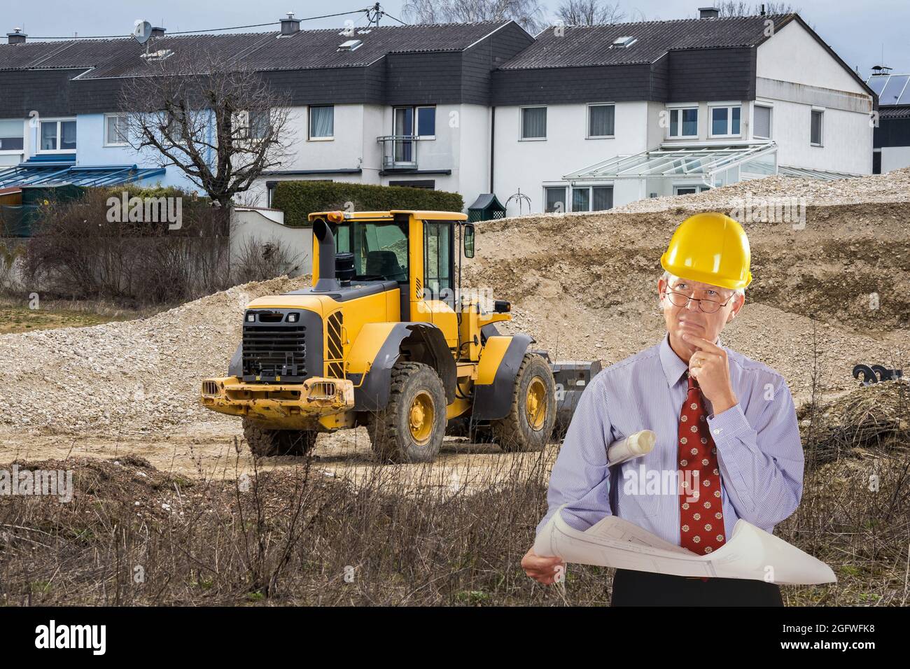 Architekt mit Bauplan und Hut, im Hintergrund Anwesen von Reihenhäusern Stockfoto