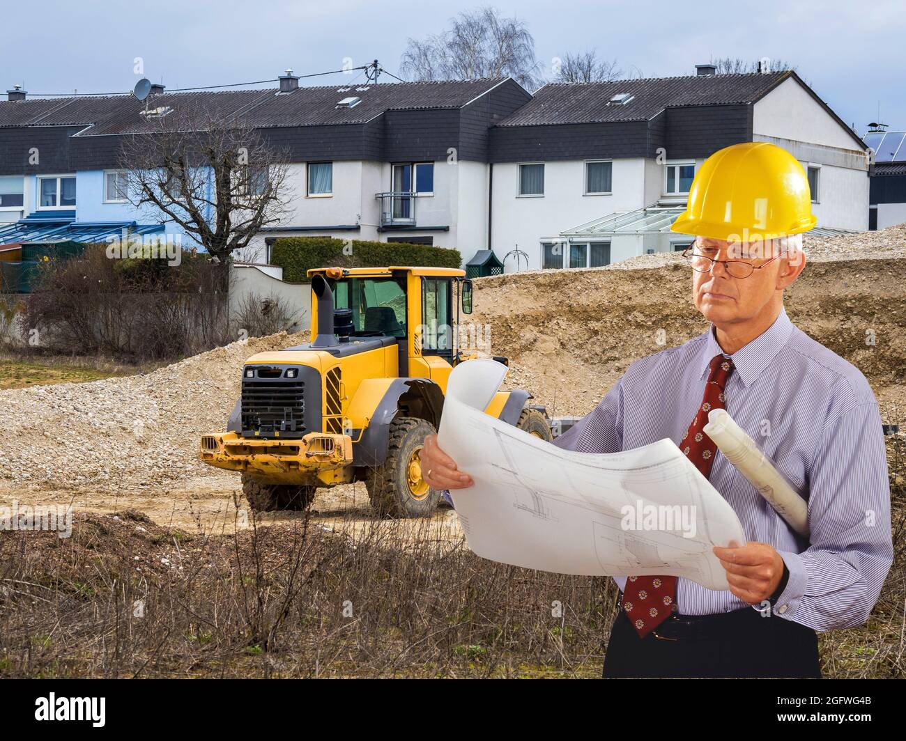 Architekt mit Bauplan und Hut, im Hintergrund Anwesen von Reihenhäusern Stockfoto