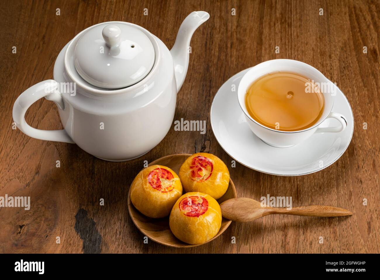 Blick aus dem hohen Winkel auf süßes chinesisches Gebäck oder Mondkuchen, gefüllt mit süßer Mungbohnenpaste und einer weißen Tasse heißen Tees aus Keramik auf einem Holzbrett. Stockfoto