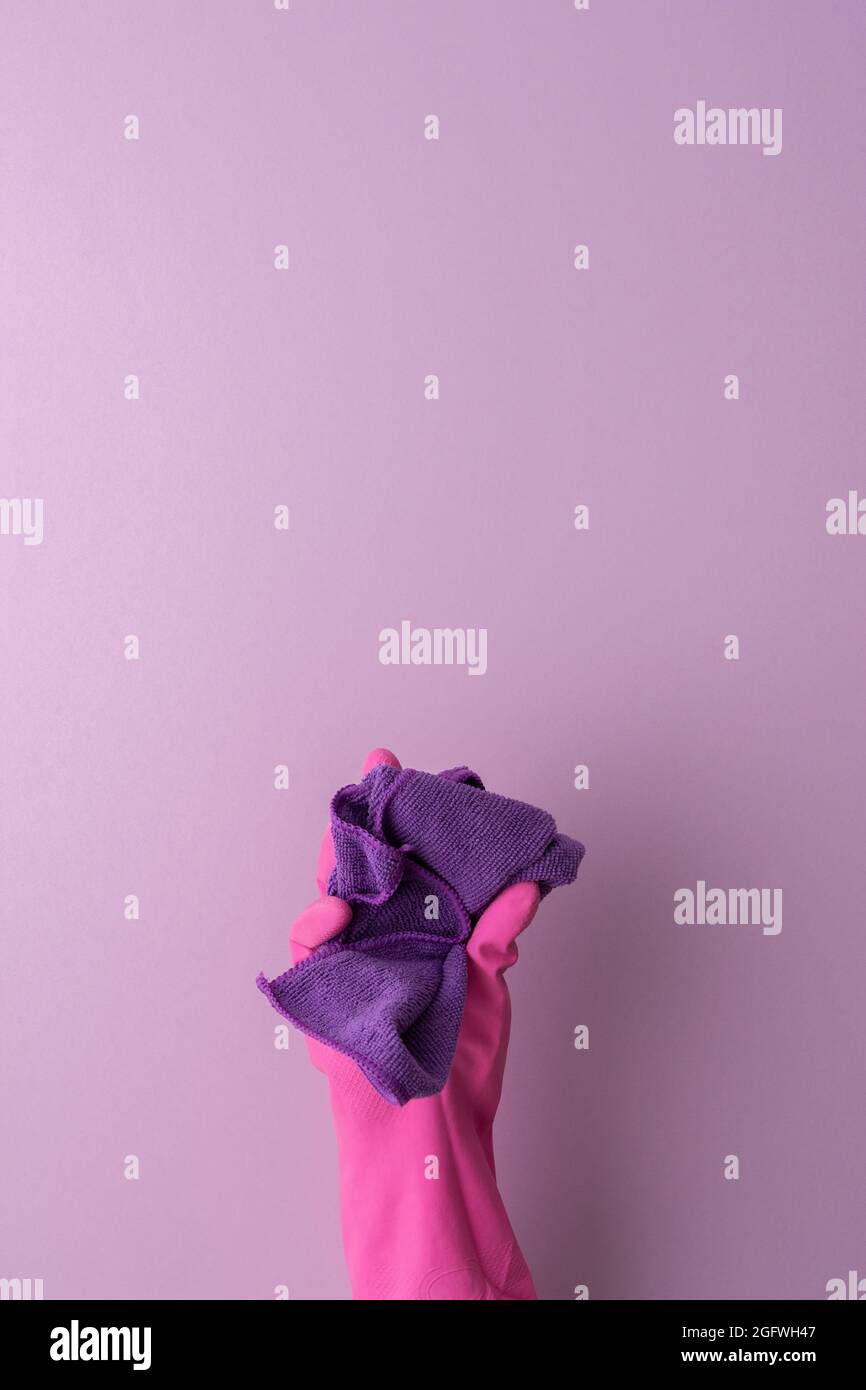 Eine Hand in einem rosa Schutzhandschuh aus Gummi hält ein Mikrofasertuch zum Waschen auf einem violetten Hintergrund Stockfoto