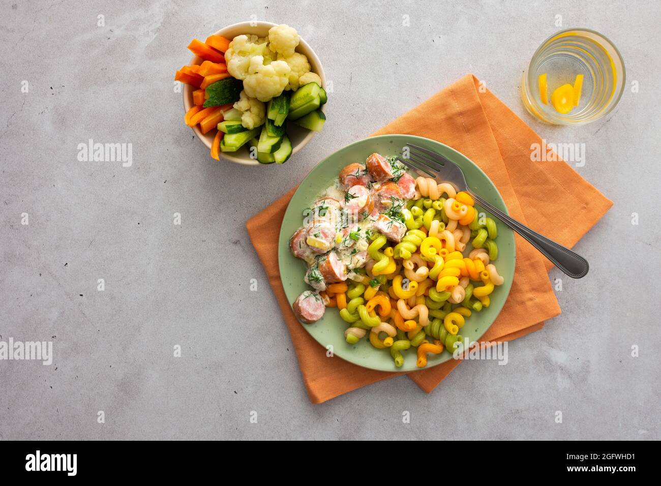 Bunte Pasta mit gekochten Würstchen in saurer Rahmsoße, frischem Gemüse und gekochtem Blumenkohl, Wasser mit Kumquats Stockfoto