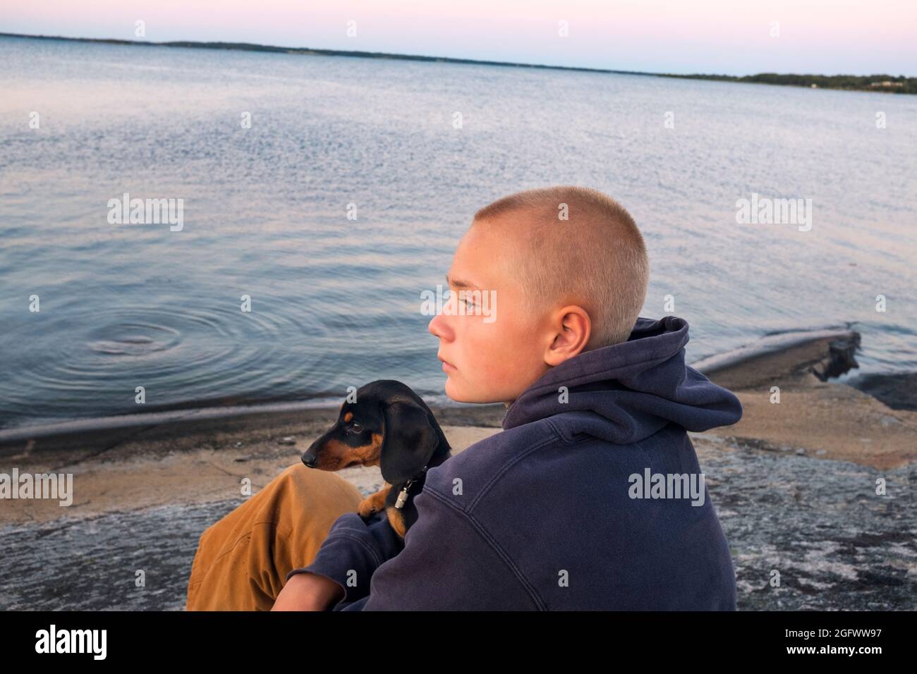 Junge mit Welpen, der auf das Meer schaut Stockfoto