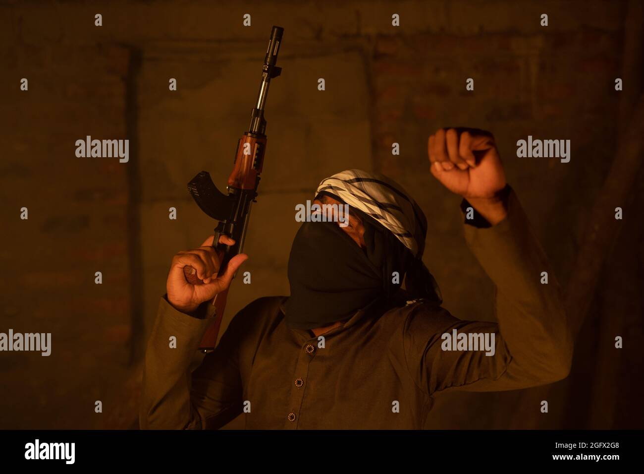 Glücklicher islamischer Kämpfer oder Soldat mit Gesichtsbedeckung, der mit einer Waffe in der Hand für den Sieg im Krieg tanzt Stockfoto