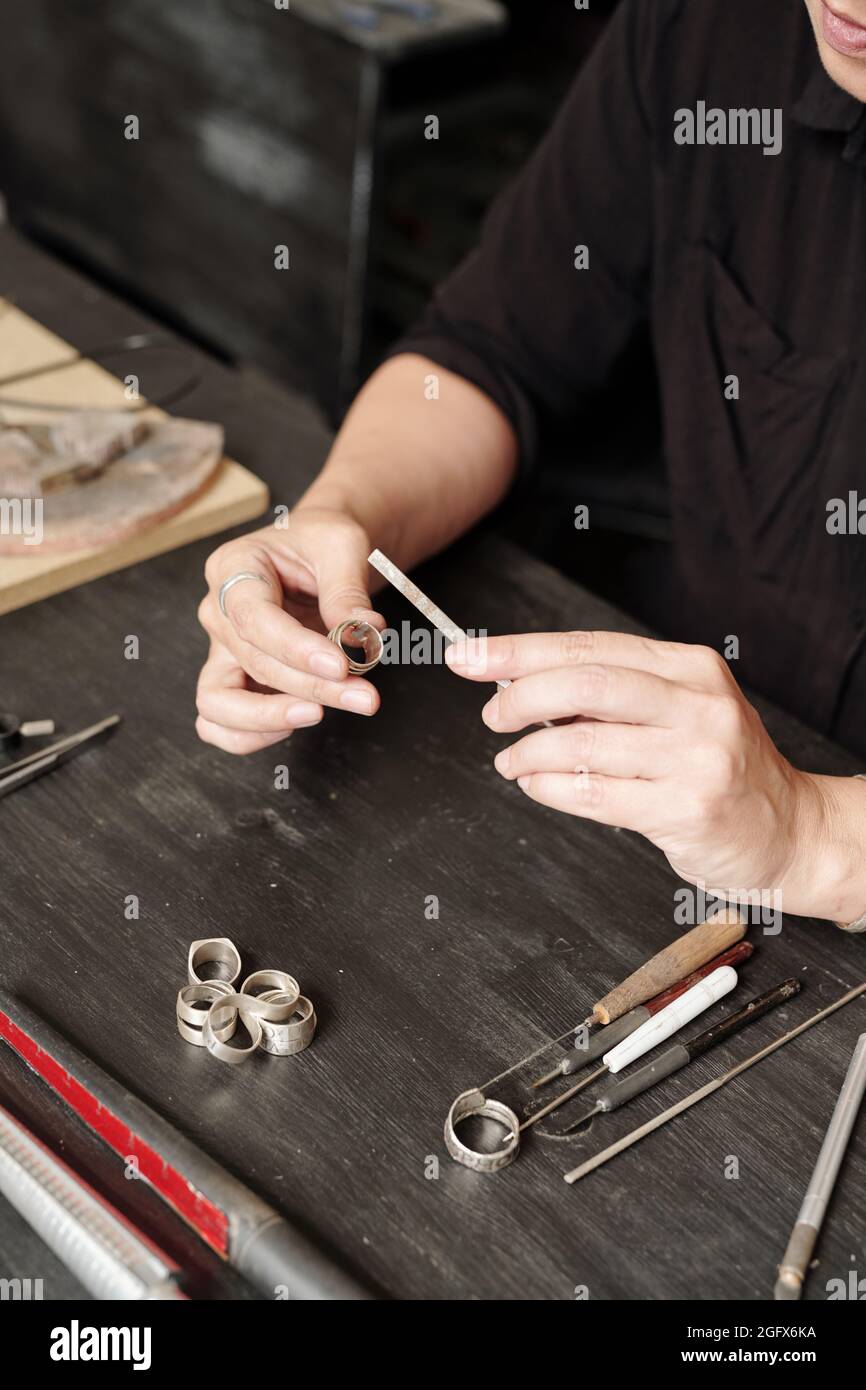 Nahaufnahme einer nicht erkennbaren Juwelierin, die am Tisch sitzt und einen Polierring mit einem Feilwerkzeug verwendet Stockfoto