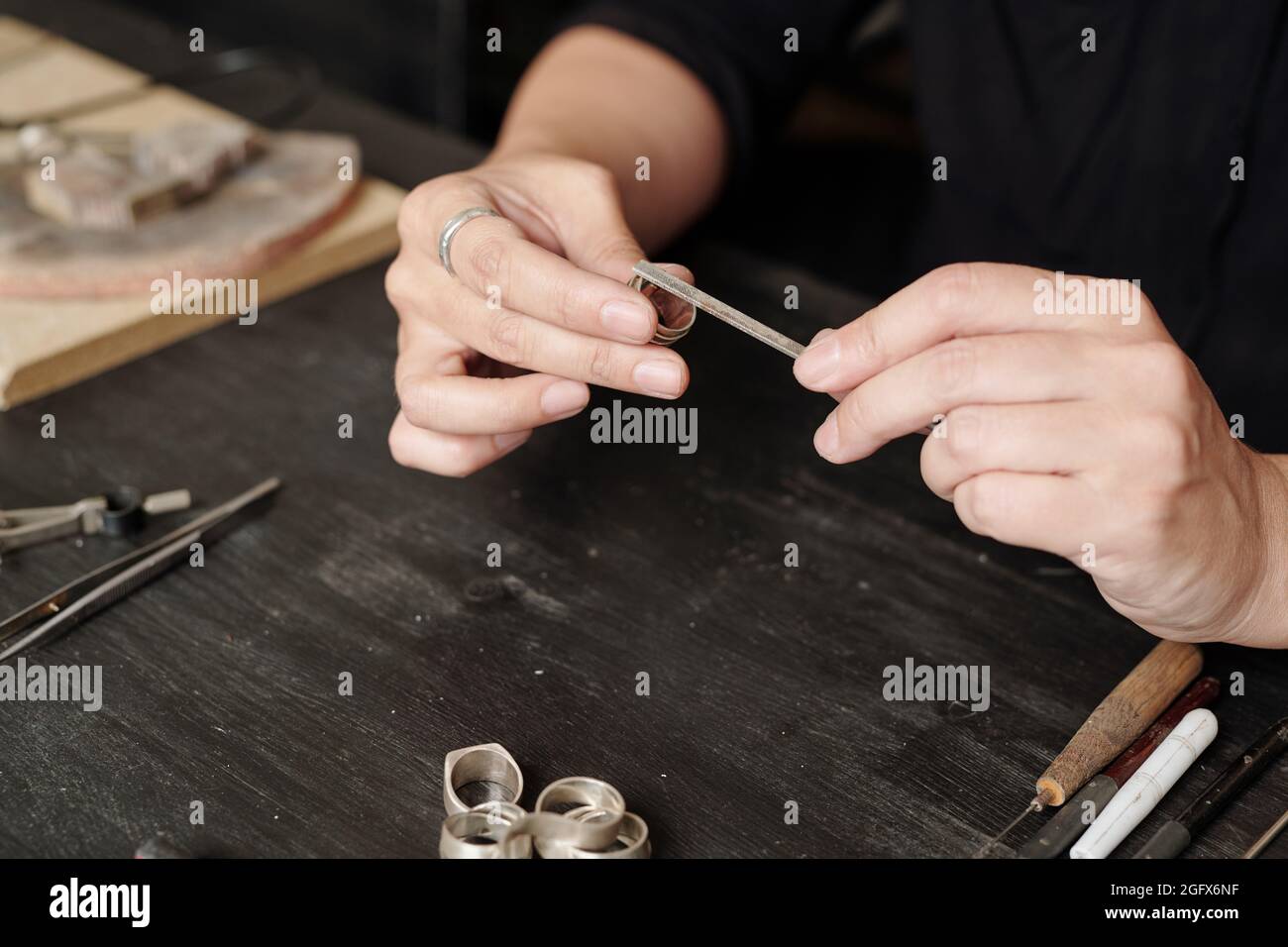 Nahaufnahme einer nicht erkennbaren Juwelierin, die am Schreibtisch sitzt und mit einer Handfeile einen handgefertigten Ring herstellt Stockfoto