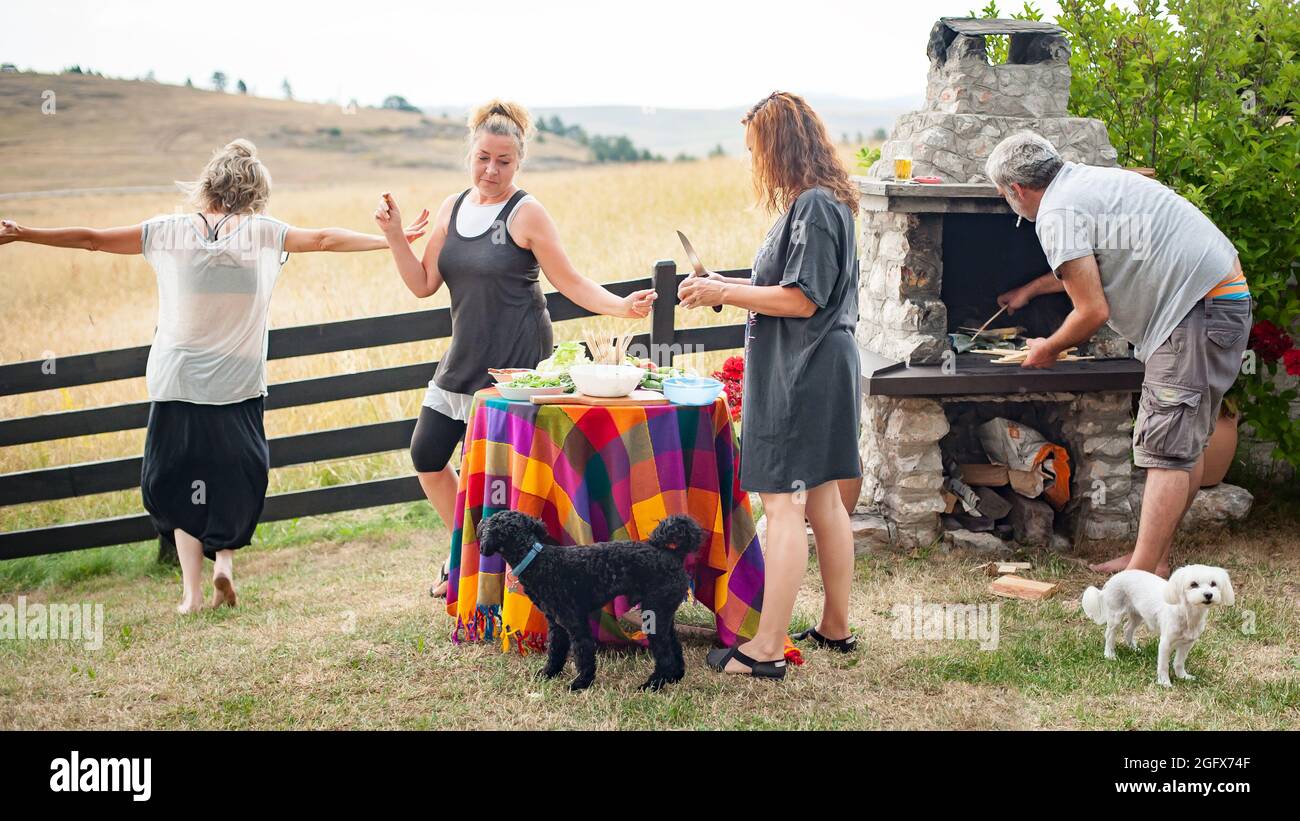 Fröhliche und verspielte Freunde lachen, tanzen und genießen das Bergambiente und grillen vor ihrem Haus Stockfoto