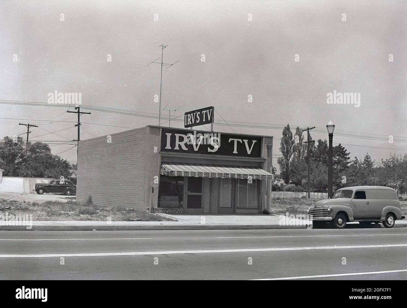 Ein amerikanischer Van der damaligen Zeit, der auf einer Straße vor einem einstöckigen Gebäude stand, wahrscheinlich ein kleines Büro namens Irv's TV, USA. Die Zahl der Amerikaner, die ein Fernsehgerät besitzen, stieg von 9 % im Jahr 1950 auf 86 % im Jahr 1959, so dass die Möglichkeiten für den Handel mit Second-Hand-Fernsehgeräten enorm waren. Stockfoto
