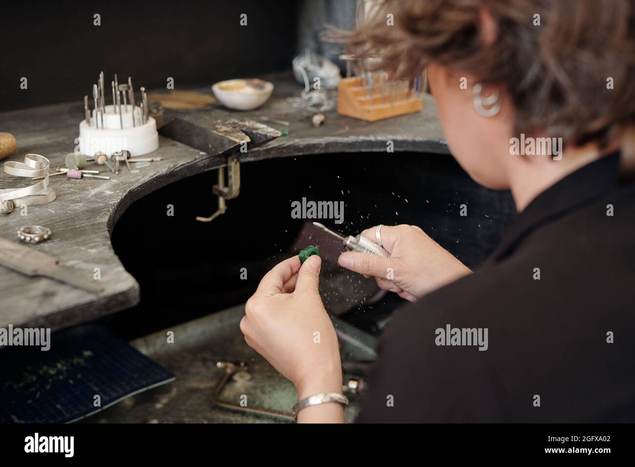 Über die Schulter schauen, wie die Kunsthandwerkerin beim Arbeiten mit Schmuck in der Werkstatt Polierer verwendet Stockfoto