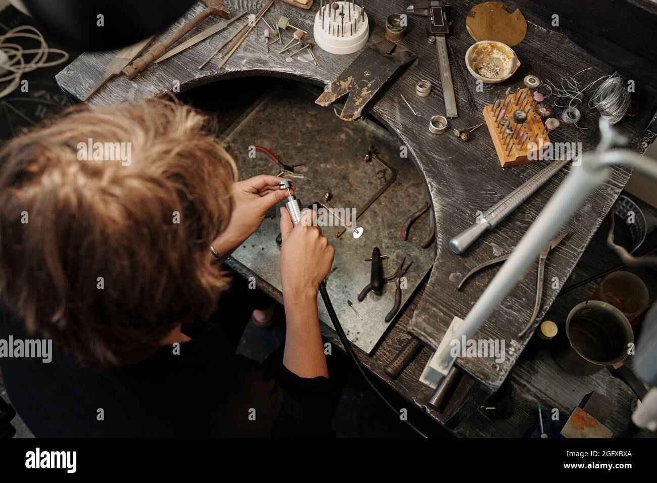 Hochwinkelansicht des Juweliers mit Schleifwerkzeug beim Polieren von Silberringen auf dem Arbeitsplatz Stockfoto