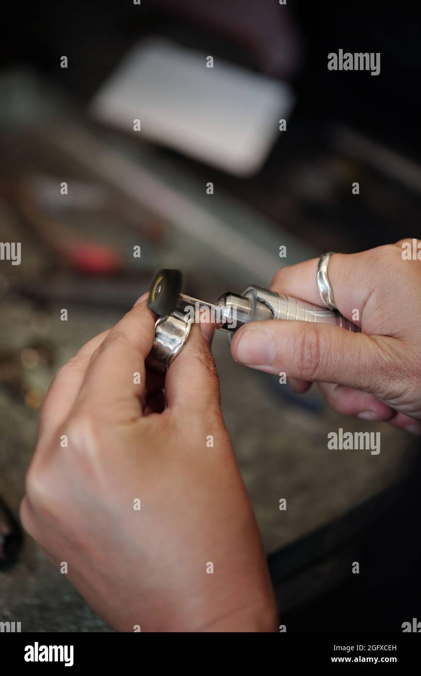 Hände von Bank Juwelier mit Schleifpolierer während der Herstellung von Silberschmuck in der Werkstatt Stockfoto