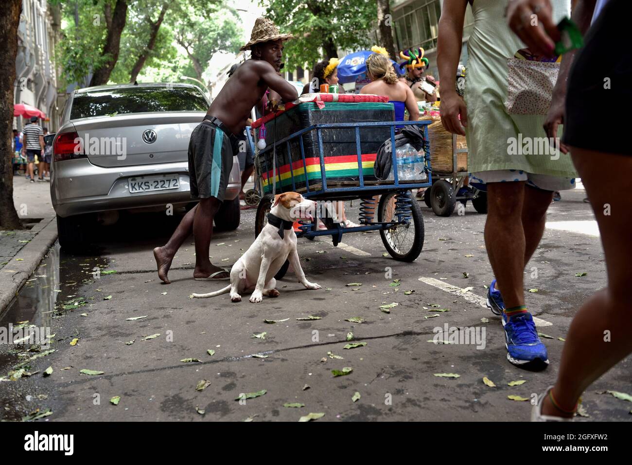 Brasilien - 16. Februar 2020: Ein Straßenverkäufer, der von seinem Hund unterstützt wird, verkauft erfrischende Getränke während einer Straßenkarnevalsumade in der Innenstadt von Rio de Janeiro. Stockfoto
