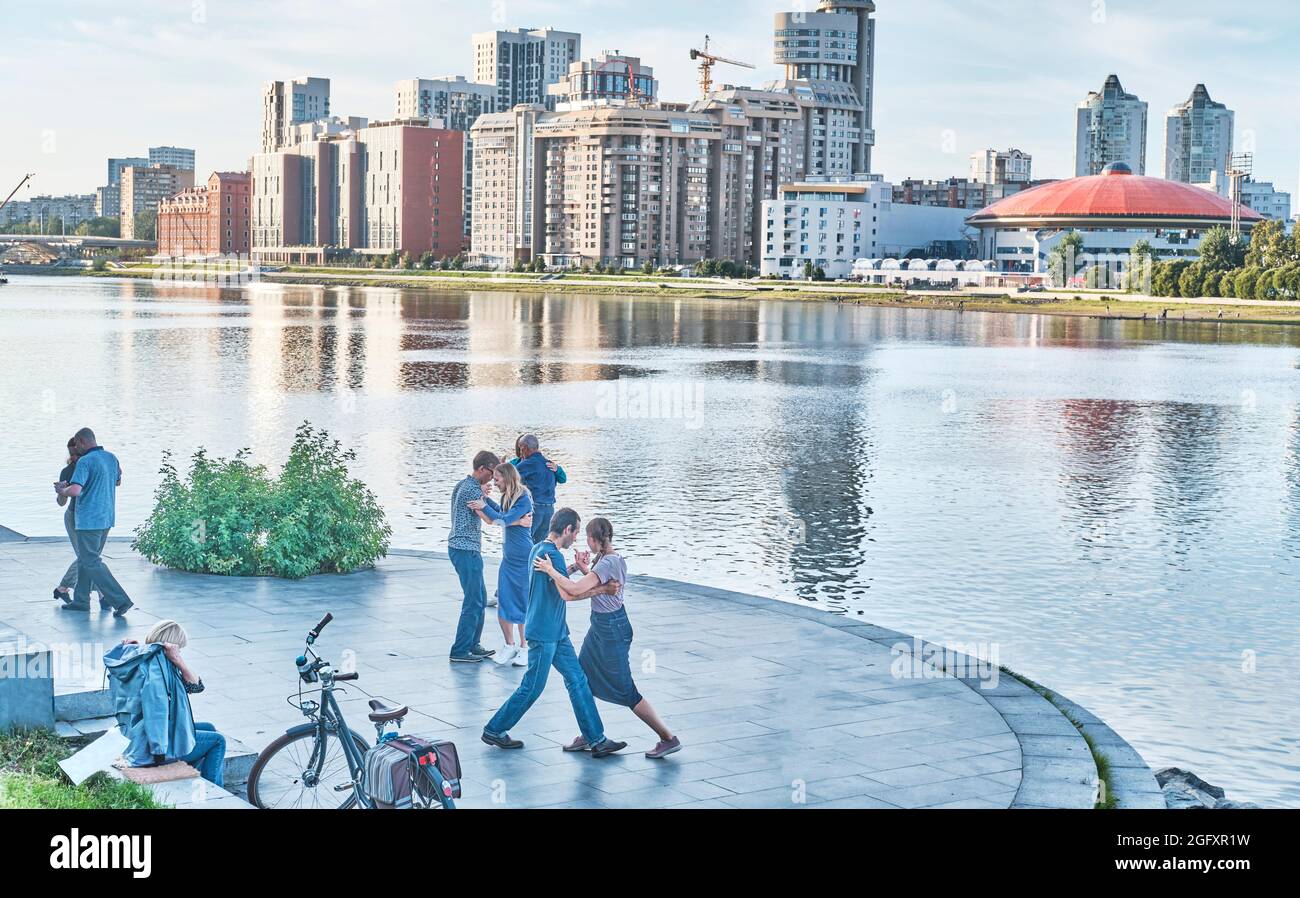 Erwachsene Paare tanzen auf dem Ufer des Flusses Iset über dem Hintergrund der Stadtgebäude. Stockfoto